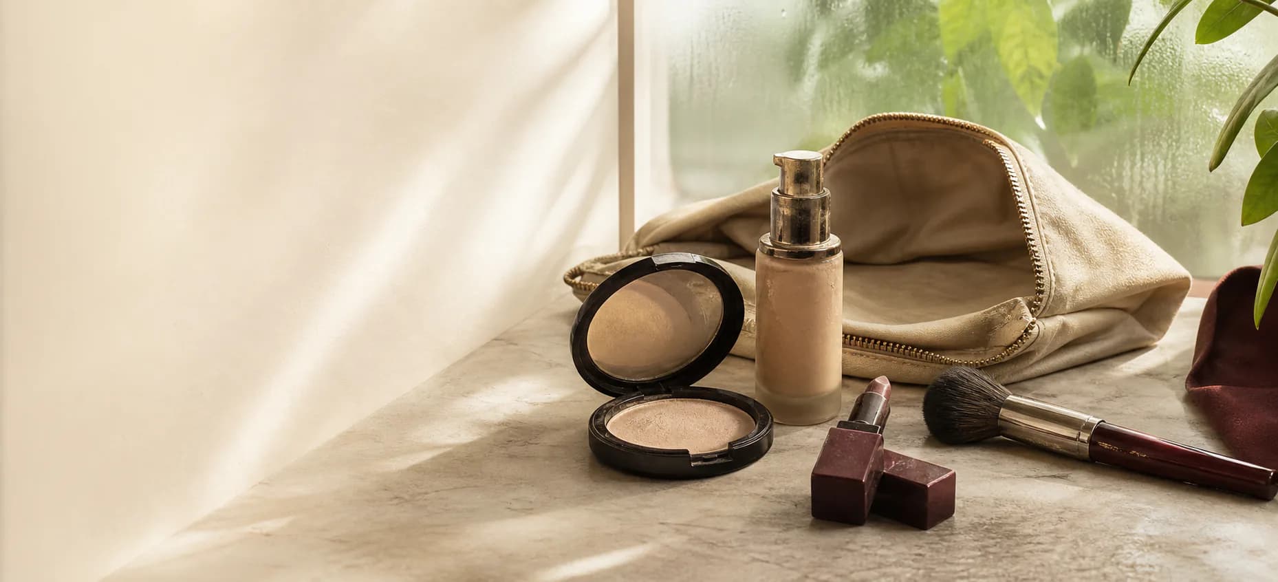 A small group of well-used makeup products beside a softly lit morning window.